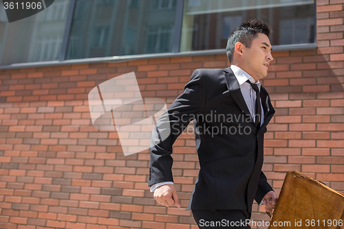 Image of Chinese young businessman running in a city street