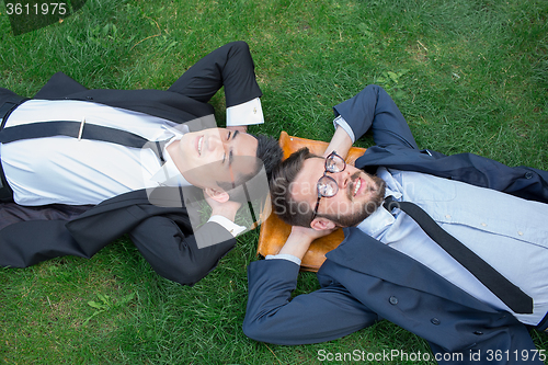 Image of The two happy young businessmen in a suit lying on the green grass