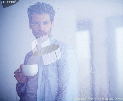 Image of relaxed young man drink first morning coffee withh rain drops on