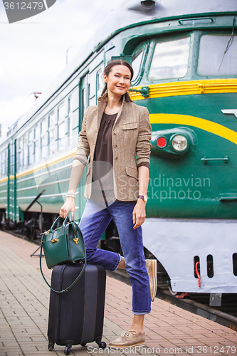 Image of smiling middle-aged woman with luggage near old train