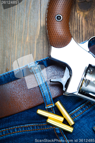 Image of silvery revolver nagant with cartridges on old blue jeans