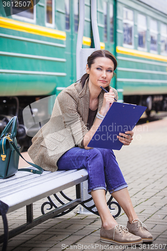 Image of beautiful middle-aged woman-traveler sitting on a bench, holding
