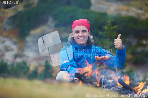 Image of hiking man prepare tasty sausages on campfire