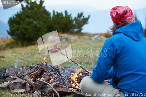 Image of hiking man prepare tasty sausages on campfire