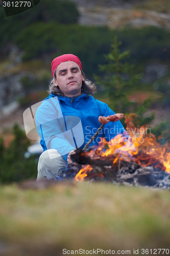 Image of hiking man prepare tasty sausages on campfire