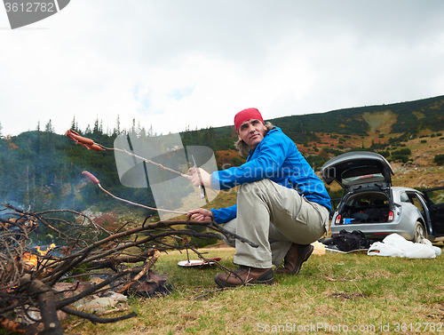 Image of hiking man prepare tasty sausages on campfire