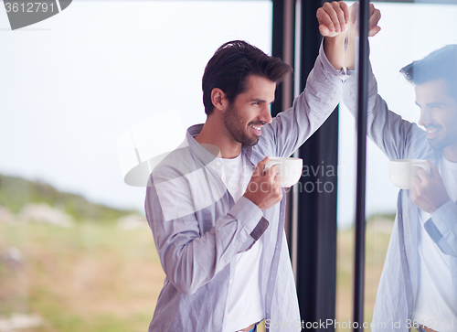 Image of relaxed young man drink first morning coffee withh rain drops on