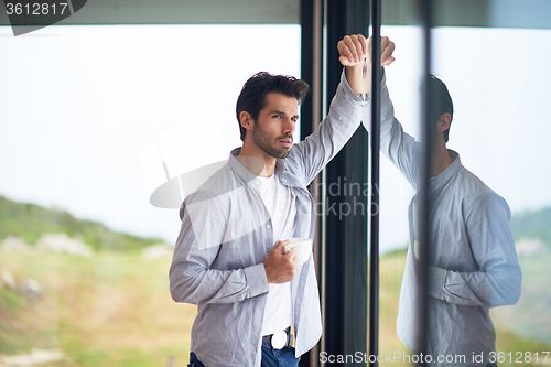 Image of relaxed young man drink first morning coffee withh rain drops on