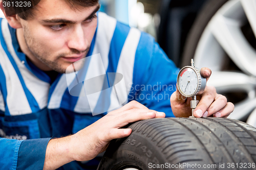 Image of Mechanic, checking the wear on the tread of a tire