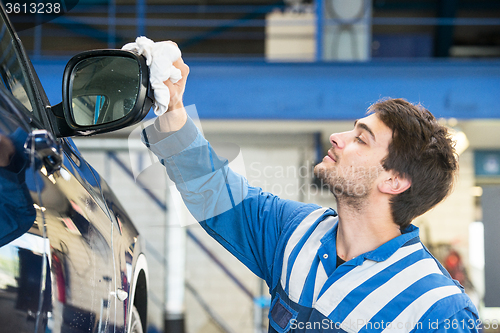 Image of Mechanic, taking pride in his work, polishing the side mirror ho