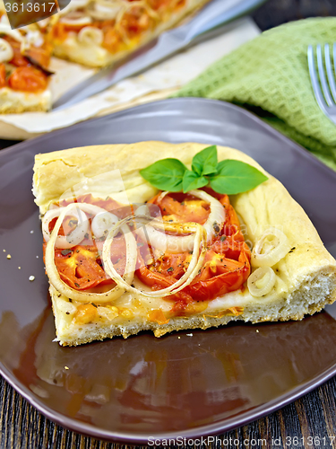 Image of Pie with onions and tomatoes in brown plate on dark board