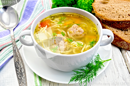 Image of Soup with meatballs and noodles in bowl on board