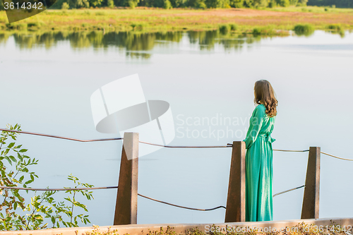 Image of A young girl stands on the bridge over the river and looks into the distance