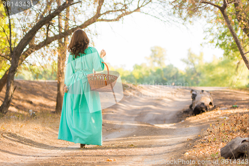 Image of A girl in a long dress holding a basket is on the road into the distance