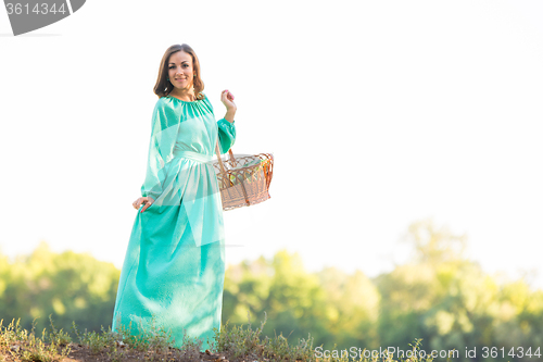 Image of The girl with a basket in a long dress standing on the hill