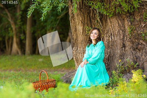 Image of A girl in a long dress sat by a tree in the woods