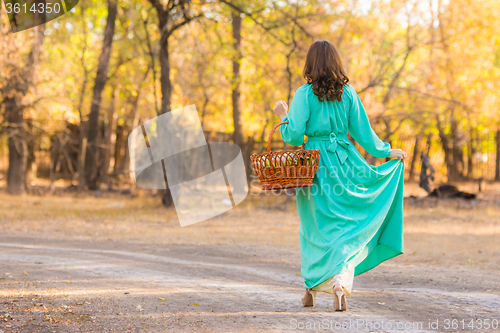 Image of A girl in a long dress walking along the road with a basket in the hands of