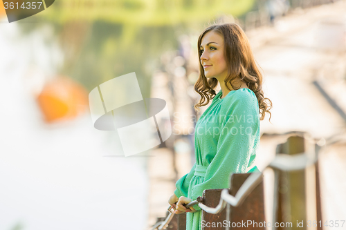 Image of Beautiful girl standing on the bridge over the river and looks into the distance