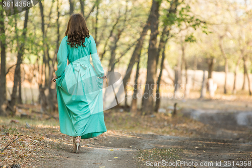 Image of A girl in a long dress walking on a forest road
