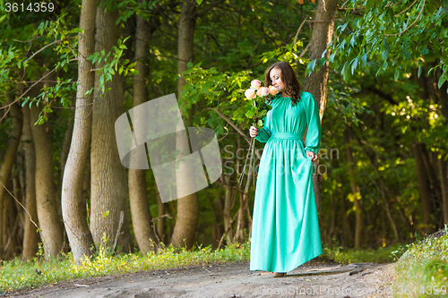 Image of A girl in a long dress walking along the road and sniffing a bouquet of roses
