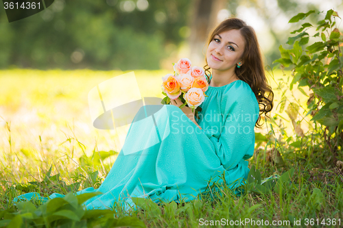 Image of A young girl sits with a bouquet of flowers under the shade of trees on a sunny day
