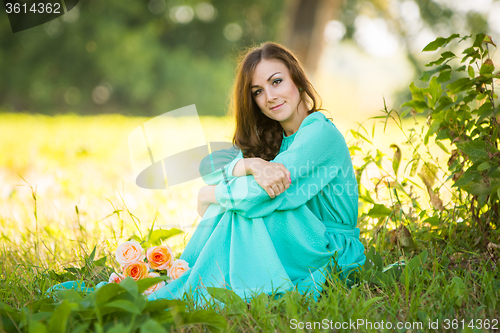 Image of A beautiful girl sitting under the shade of trees, lies at the feet of her a bouquet of roses