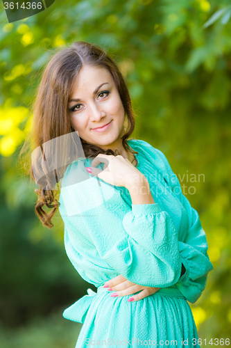 Image of Half-length portrait of a beautiful girl in a dress on a background of green foliage