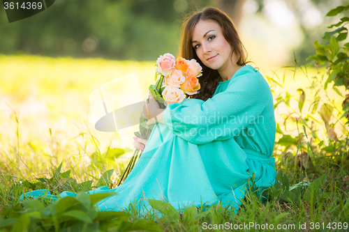 Image of Portrait of a young girl with a bouquet of roses sitting in the shade of the trees on a sunny day