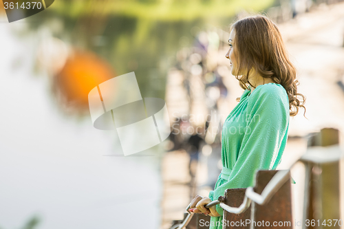 Image of Beautiful girl stopped on the bridge over the river and looked into the distance