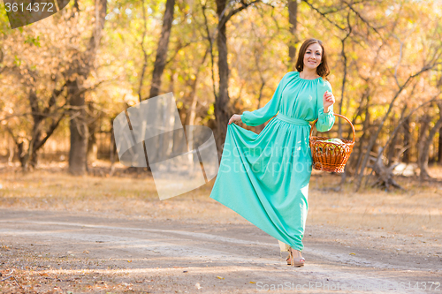Image of A girl in a long dress holding her dress and a basket of walking on the road