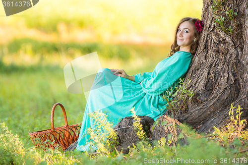 Image of A girl in a long dress sat down at the old tree in the forest