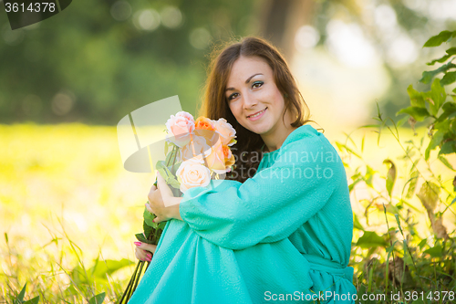 Image of Portrait of a young girl with a bouquet of roses sitting in the shade of the trees on a sunny day