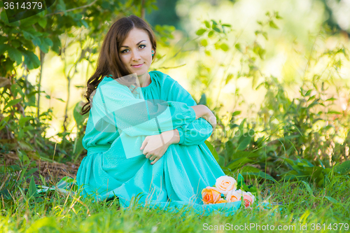 Image of A girl in a long dress sitting in the shade of the trees on a sunny day