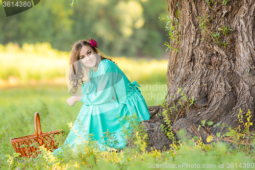 Image of A girl in a long dress in a good mood crouched near a tree in the woods