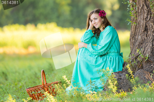 Image of A girl in a long dress and sat down at the thought of an old tree in the forest