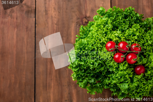 Image of lettuce salad and cherry tomatoes on a wood background