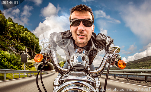 Image of Funny Biker in sunglasses and leather jacket racing on mountain 