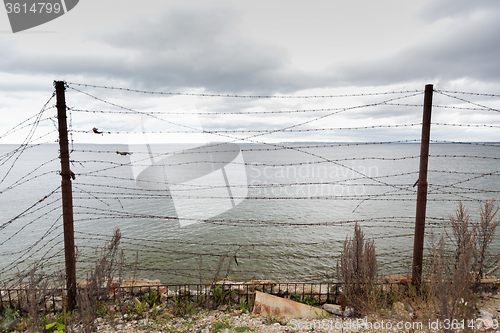 Image of barb wire fence over gray sky and sea