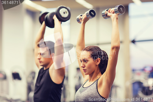 Image of smiling man and woman with dumbbells in gym