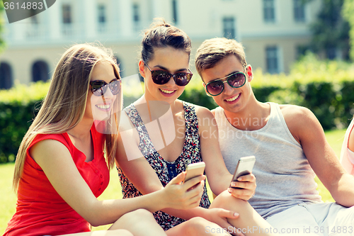 Image of smiling friends with smartphones sitting in park