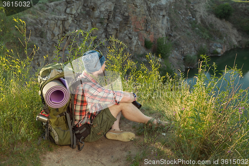 Image of Young caucasian man with backpack sitting on the top of hill