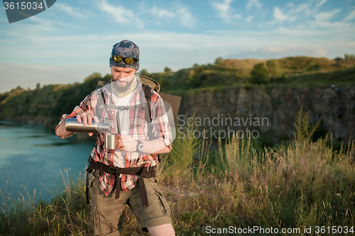 Image of Young caucasian man with backpack resting and drinking water