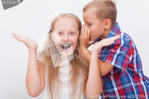 Image of Teenage boy whispering in the ear a secret to teen girl on white  background