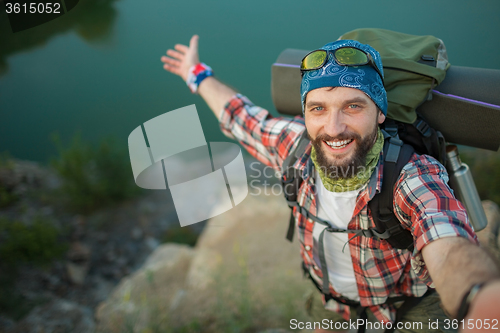Image of fully equipped tourist smiling on the background of lake