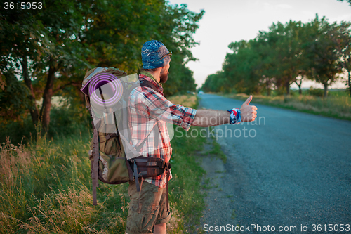 Image of Young caucasian tourist hitchhiking along a road.