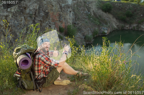 Image of Young caucasian man with backpack sitting on the top of hill
