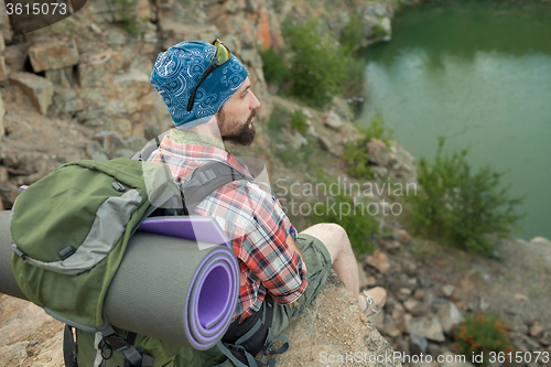 Image of Young caucasian man with backpack sitting on the top of hill