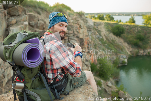 Image of Young caucasian man with backpack sitting on the top of hill