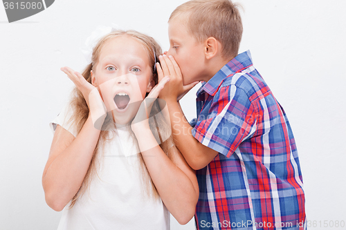 Image of Teenage boy whispering in the ear a secret to teen girl on white  background