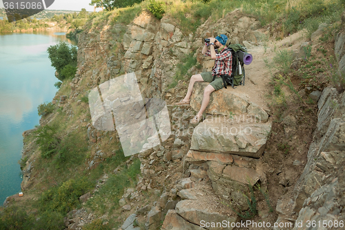 Image of Young caucasian man with backpack sitting on the top of hill